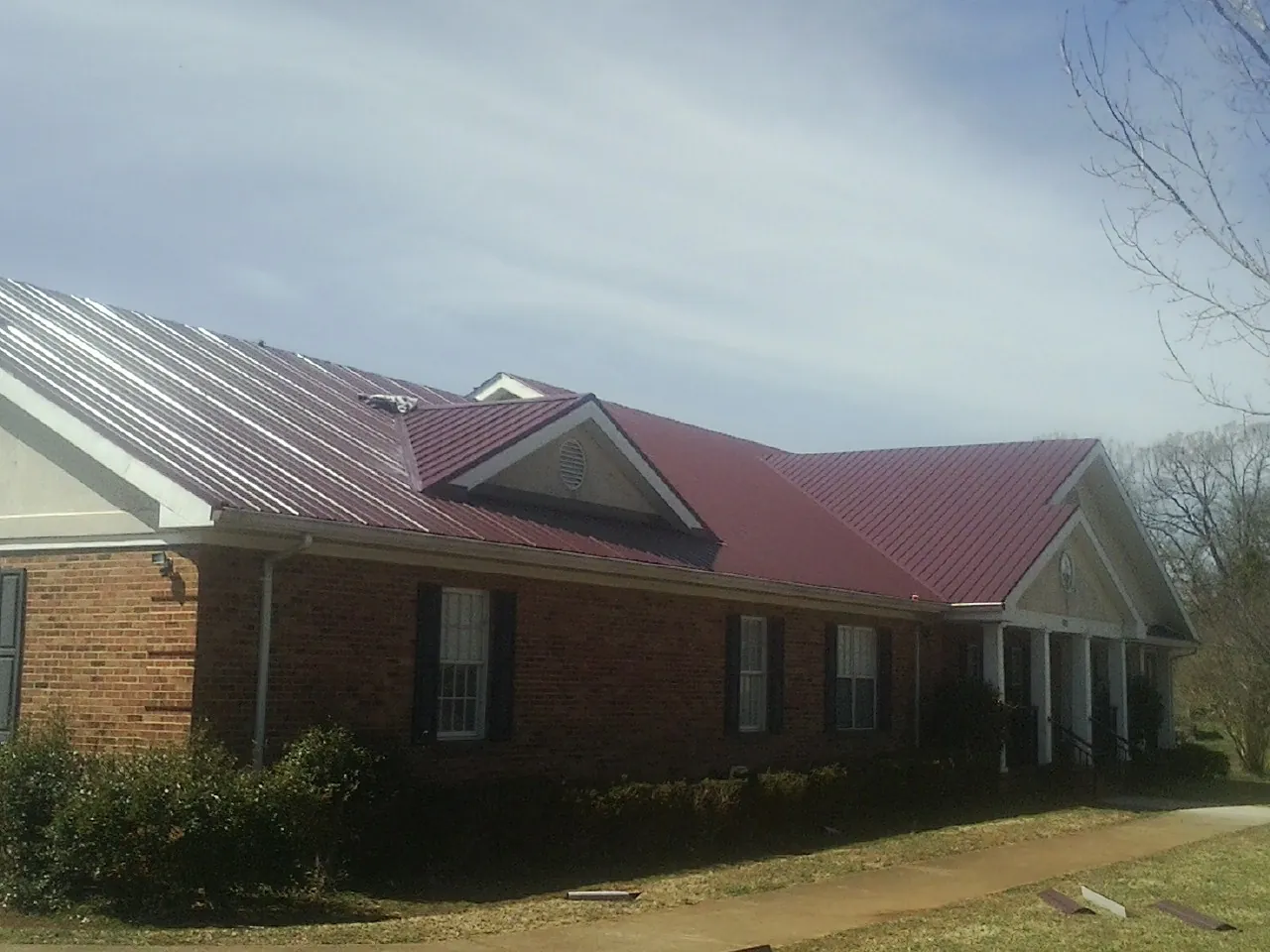 Red metal roof with gabled entries on a long brick building, from a Hail Damage Roof Repair job in Union Mills