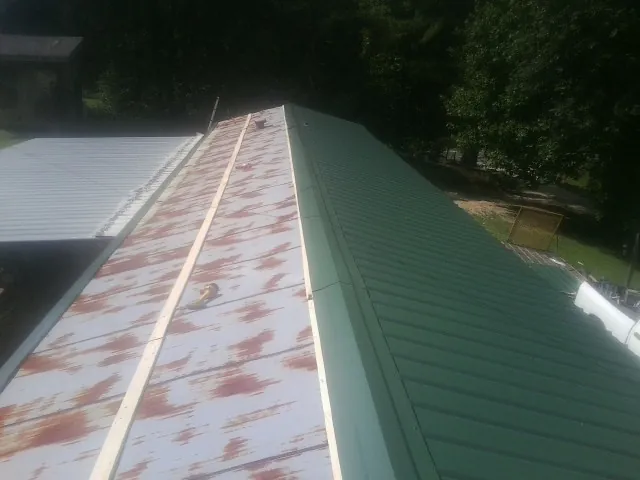 Old rusted panels beside newly installed green metal roofing — Wind Damage Roof Repair by Roofing Brothers in Union Mills