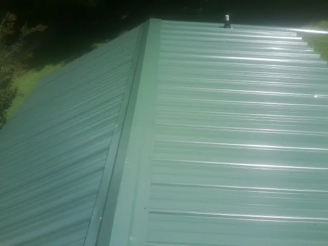 New green metal panels meeting at the ridge of a roof — Flat Roof Repair work by our crew in Union Mills