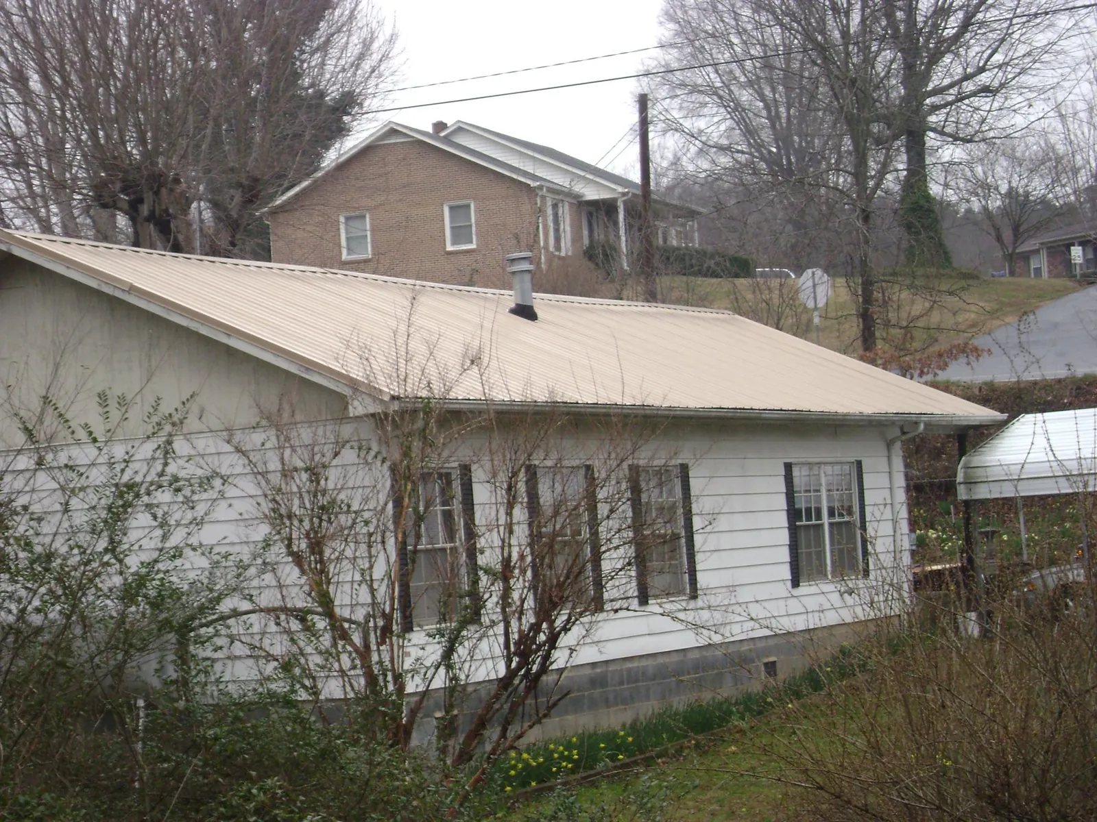 Tan metal roof on a white sided house set into a hillside — Commercial Roofing by Roofing Brothers in Union Mills